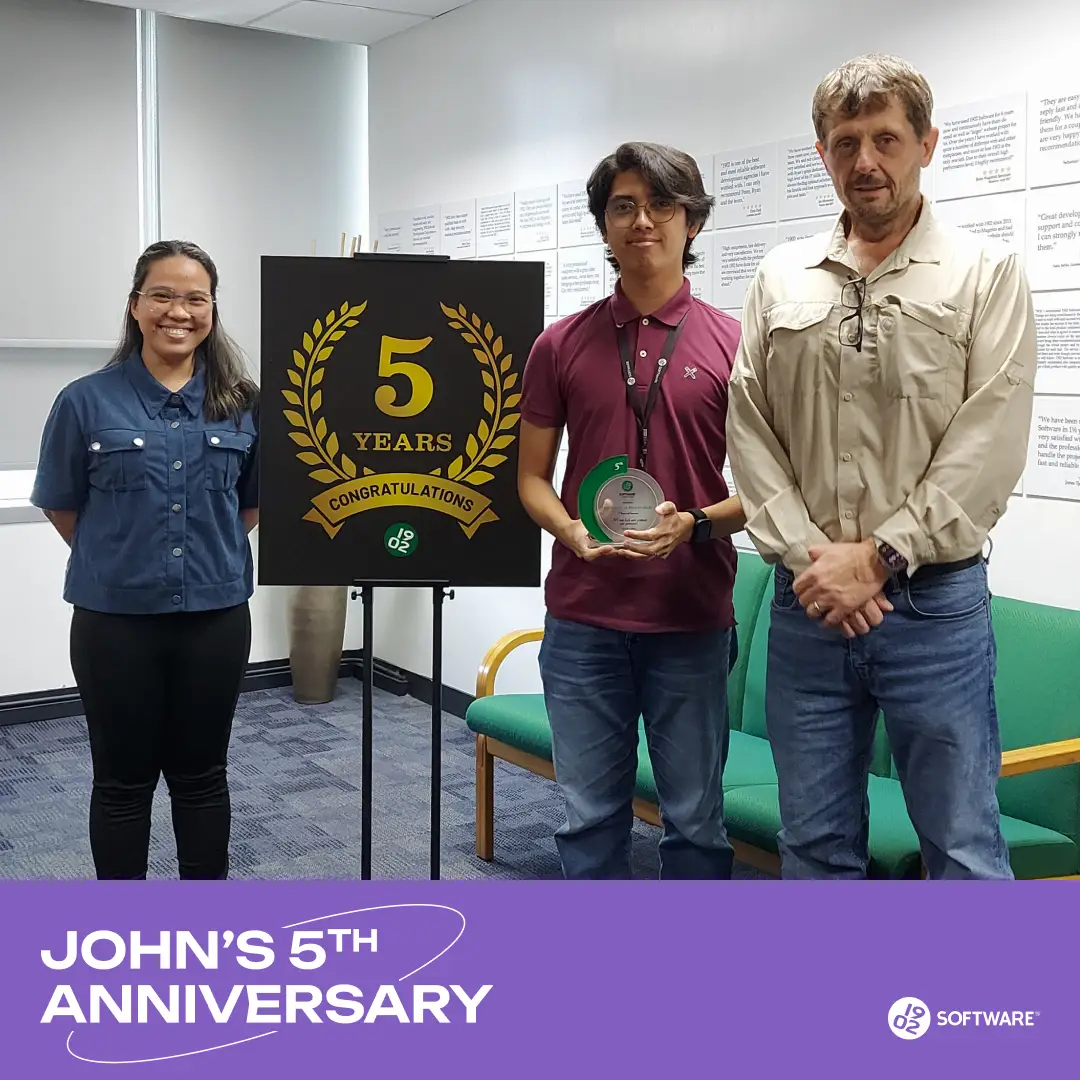Three people standing beside a sign reading "5 Years Congratulations" celebrating John's 5th anniversary at 1902 Software.