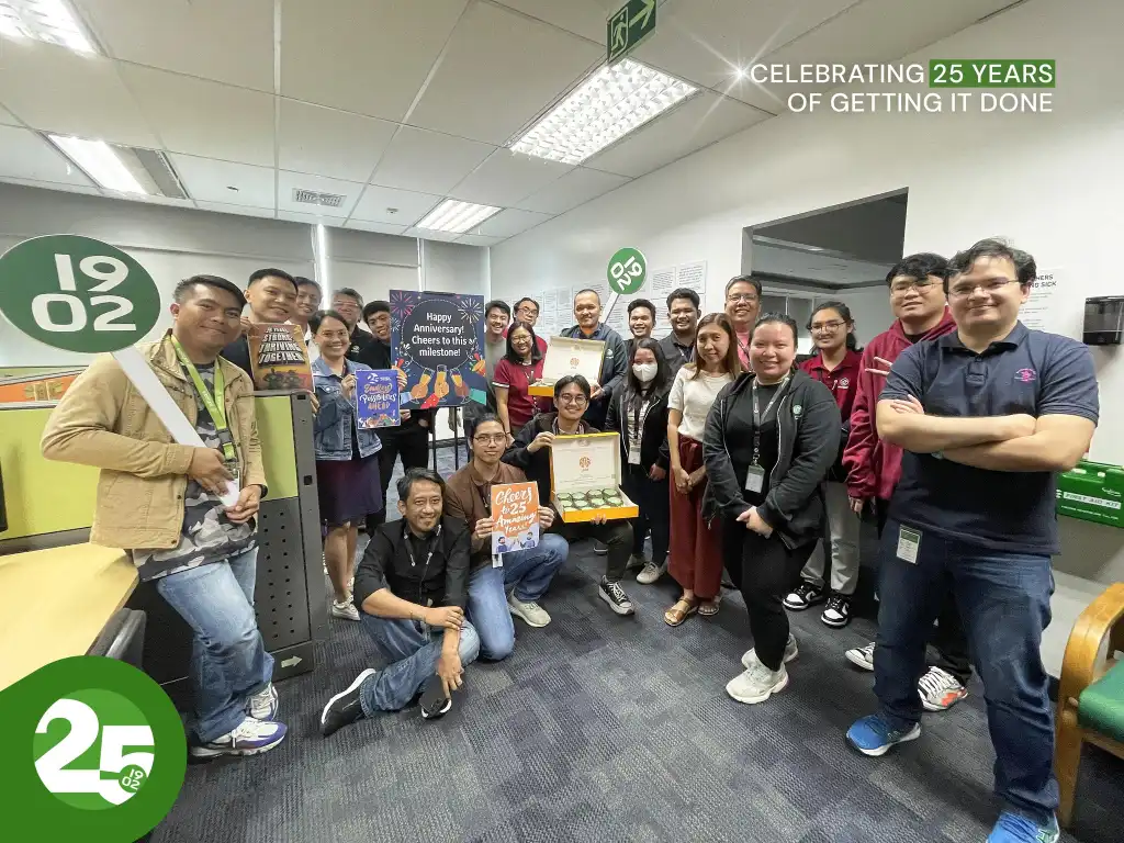 1902 Software team celebrating 25th anniversary with signs, certificates, and donuts in office, text "Celebrating 25 years of getting it done"