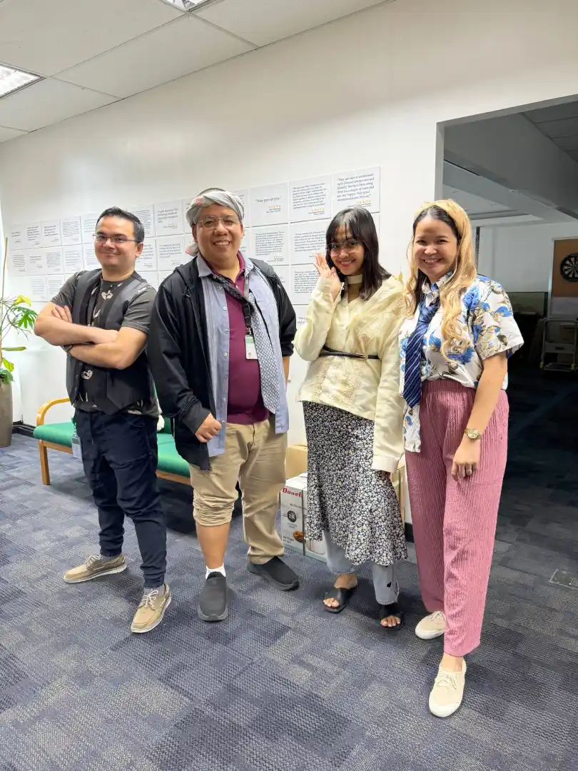 Four colleagues standing in an office with white walls and motivational quotes displayed behind them.