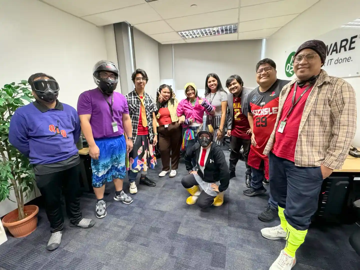 Group of 10 people in colorful casual and costume attire posing in an office room with a 1902 Software banner on the wall.
