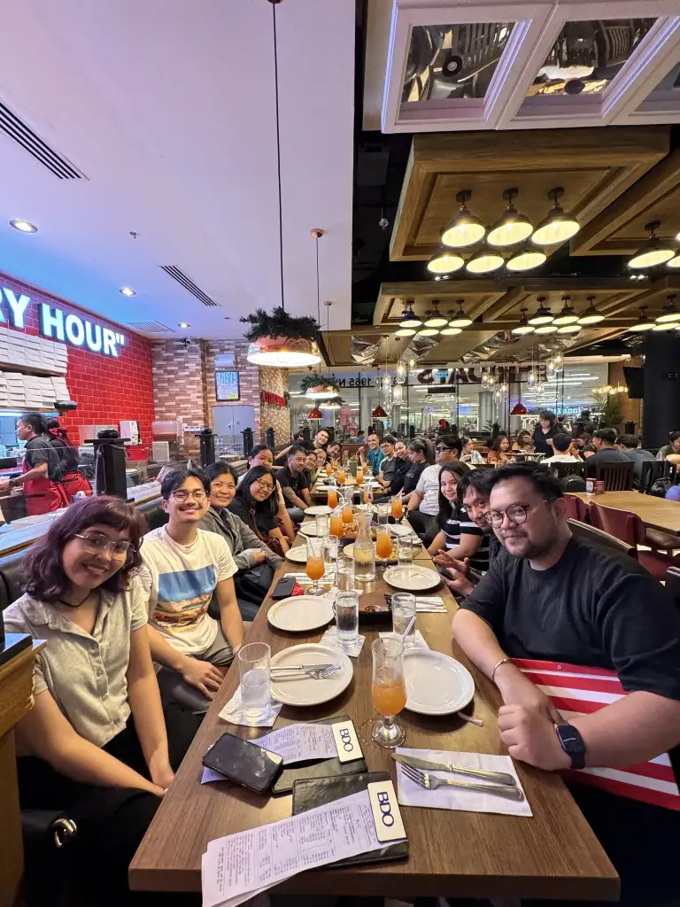 Marketing and design team gathered around a long table at a restaurant for a team-building dinner with drinks and menus visible.