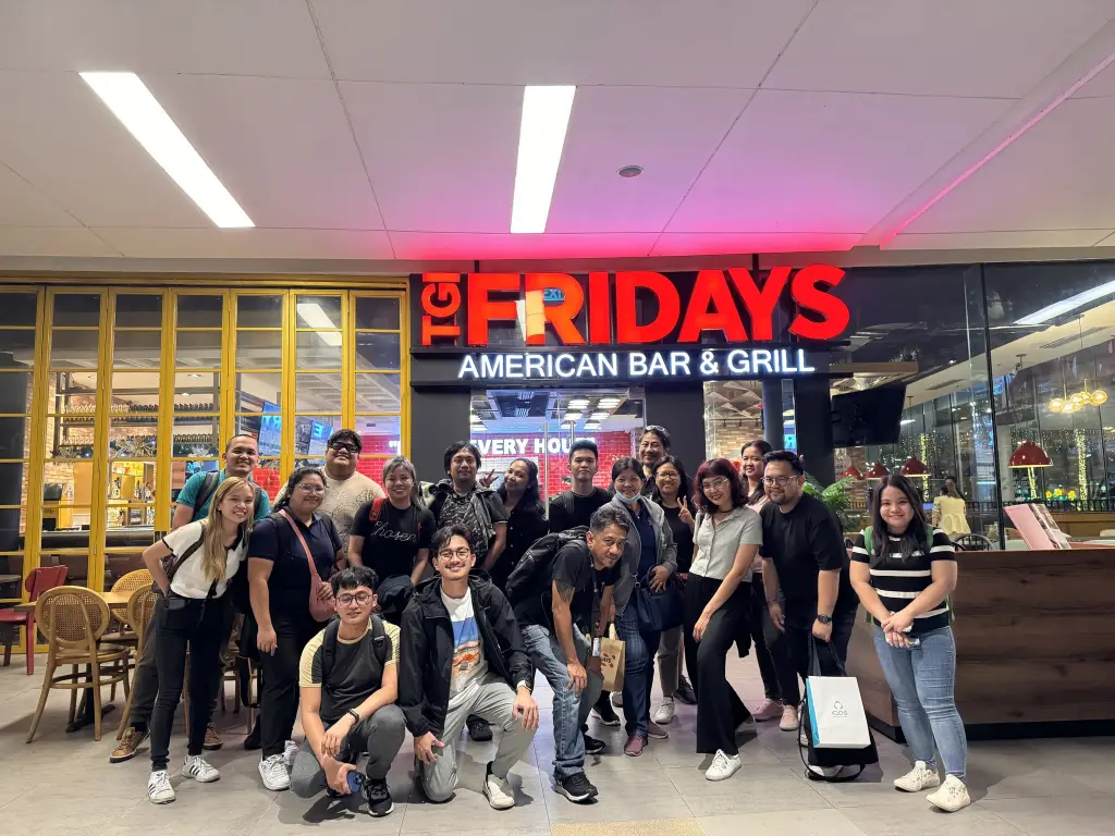 Group of people posing in front of TGI Fridays American Bar & Grill during a team-building event.