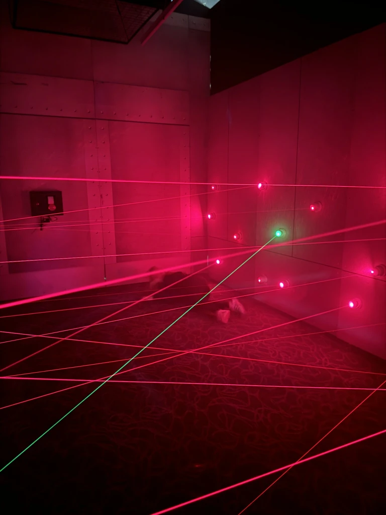 Person crawling on floor through red and green laser beams in a dark room during team-building activity