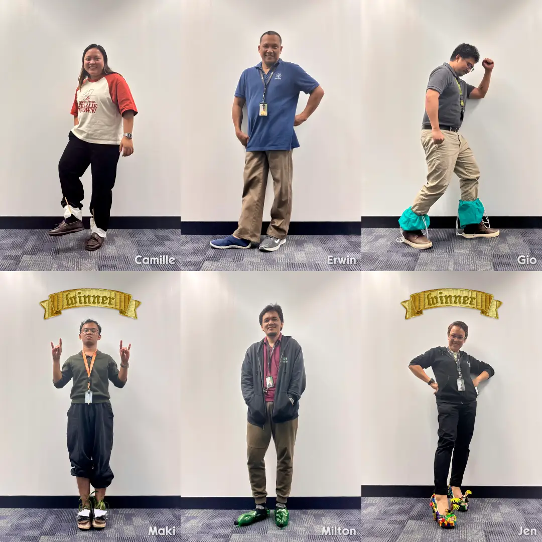 Six team members posing against a white wall, three wearing shoe covers or unique footwear; Maki and Jen have "winner" banners above them.