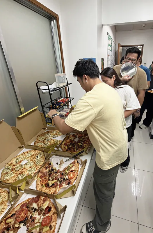 A close-up view of employees picking out pizza slices from various open boxes, including a spinach and cheese pizza and a supreme pizza.